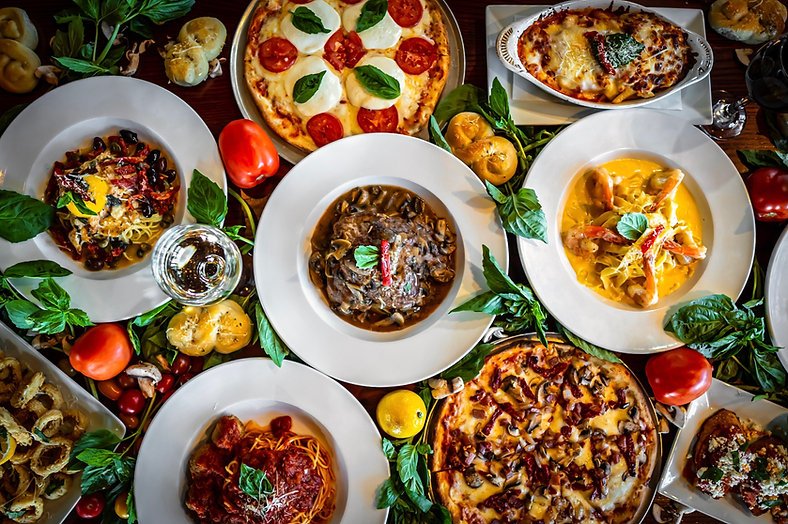 A table spread with pizzas, pastas, chicken marsala, and garlic knots